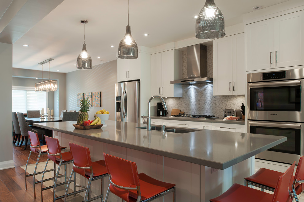 Large modern galley kitchen/diner in Toronto with a submerged sink, shaker cabinets, white cabinets, engineered stone countertops, grey splashback, mosaic tiled splashback, stainless steel appliances, an island, porcelain flooring and white floors.