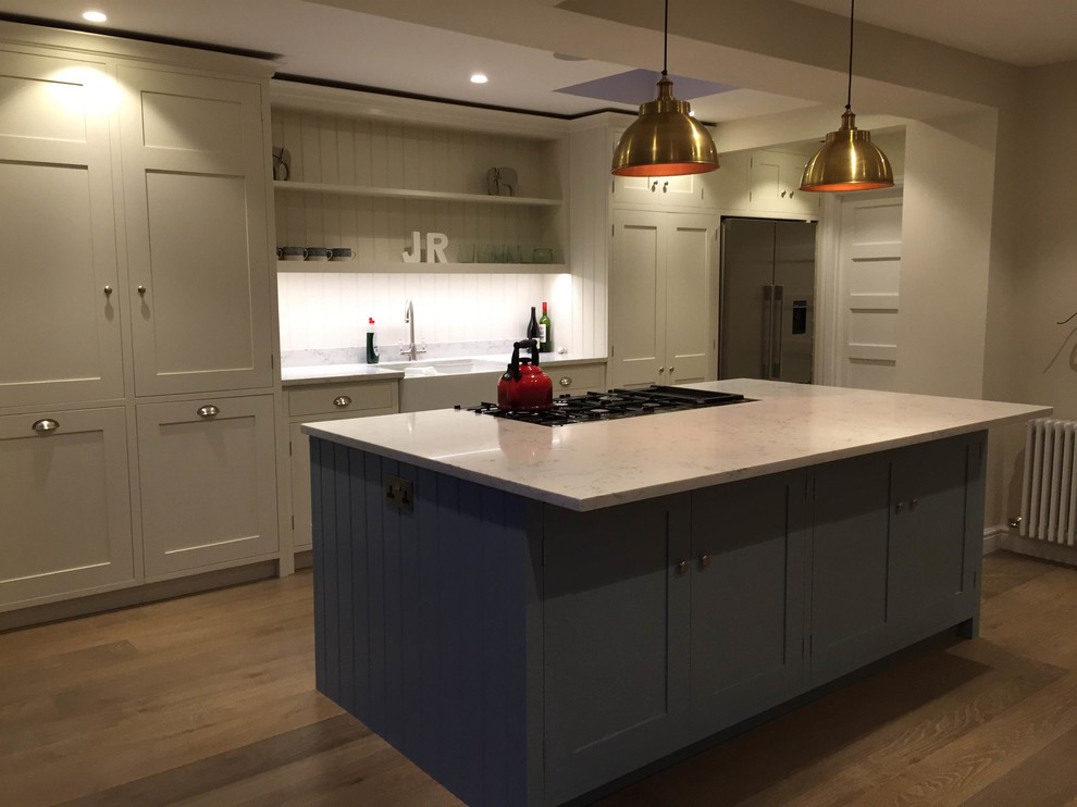 Photo of a medium sized traditional single-wall open plan kitchen in Surrey with a double-bowl sink, shaker cabinets, blue cabinets, quartz worktops, white splashback, stainless steel appliances and an island.