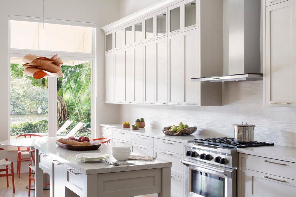 Large trendy l-shaped medium tone wood floor open concept kitchen photo in Miami with an integrated sink, shaker cabinets, gray cabinets, quartzite countertops, beige backsplash, porcelain backsplash, stainless steel appliances and an island