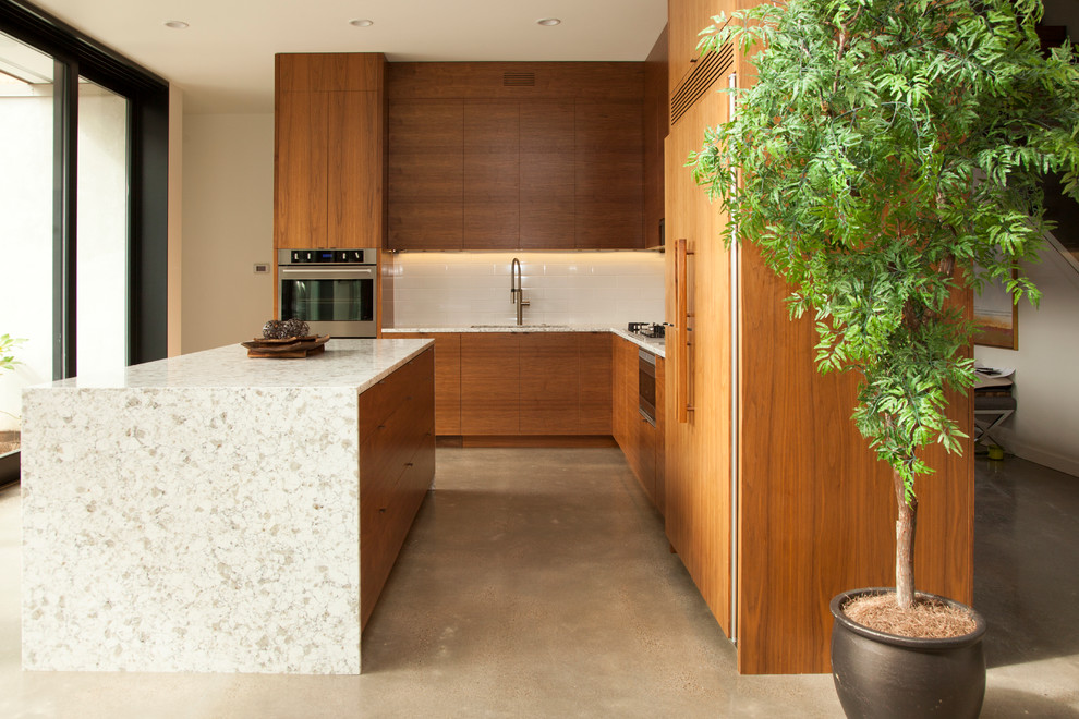 Стильный дизайн: угловая кухня среднего размера в стиле модернизм с обеденным столом, плоскими фасадами, фасадами цвета дерева среднего тона, белым фартуком, фартуком из плитки кабанчик и бетонным полом - последний тренд