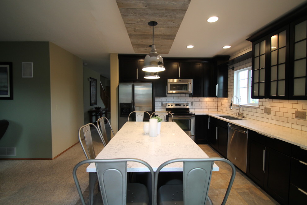 Photo of a large urban l-shaped open plan kitchen in Denver with a submerged sink, shaker cabinets, dark wood cabinets, engineered stone countertops, white splashback, metro tiled splashback, stainless steel appliances, slate flooring and an island.