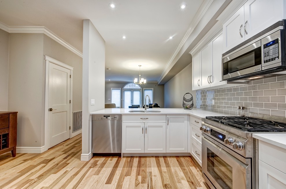 Eat-in kitchen - mid-sized contemporary l-shaped light wood floor eat-in kitchen idea in Calgary with an undermount sink, shaker cabinets, white cabinets, quartz countertops, gray backsplash, ceramic backsplash, stainless steel appliances and a peninsula