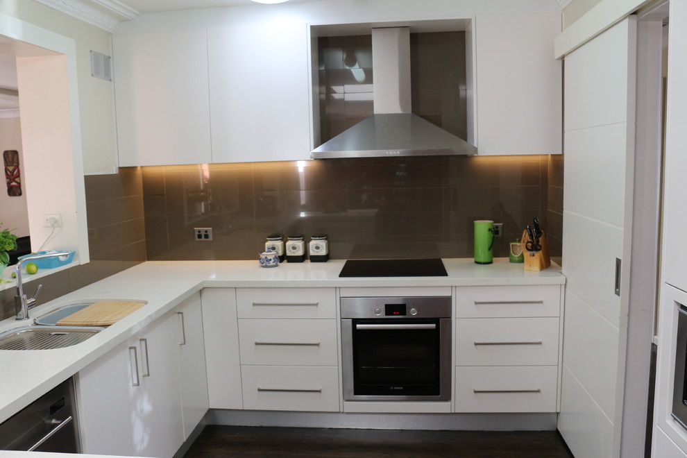 Inspiration for a large modern l-shaped open plan kitchen in Sydney with a submerged sink, flat-panel cabinets, white cabinets, engineered stone countertops, brown splashback, glass sheet splashback, stainless steel appliances, multiple islands and white worktops.