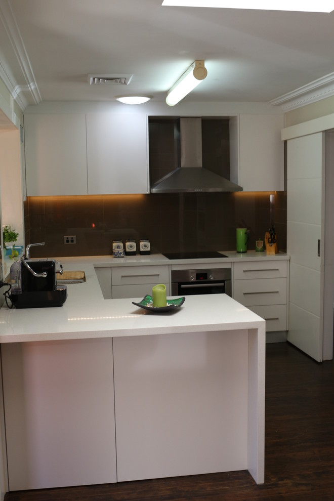 Bild på ett stort funkis vit vitt kök, med en undermonterad diskho, släta luckor, vita skåp, bänkskiva i kvarts, brunt stänkskydd, glaspanel som stänkskydd, rostfria vitvaror och flera köksöar