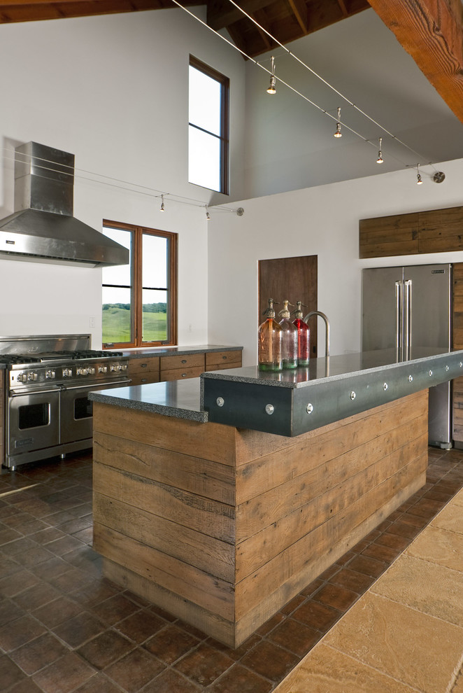 Foto på ett industriellt kök, med släta luckor, skåp i slitet trä, granitbänkskiva, rostfria vitvaror och en köksö