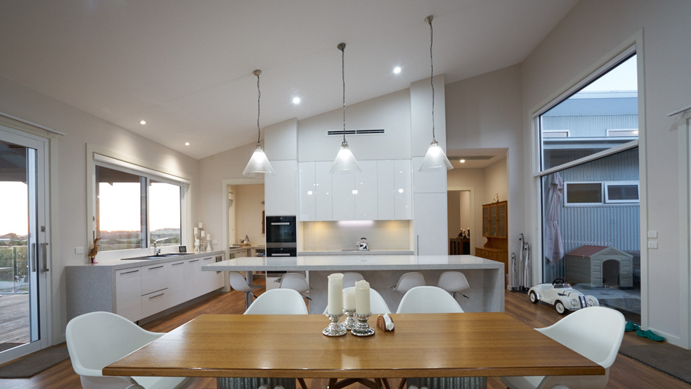 Exempel på ett mellanstort modernt grå grått kök, med en dubbel diskho, vita skåp, vitt stänkskydd, glaspanel som stänkskydd, rostfria vitvaror, en köksö, mörkt trägolv och brunt golv