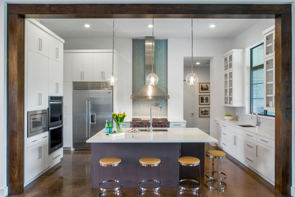 Moderne Küche mit Küchengeräten aus Edelstahl, Betonboden, Kücheninsel, Unterbauwaschbecken, flächenbündigen Schrankfronten, weißen Schränken und Küchenrückwand in Blau in Austin