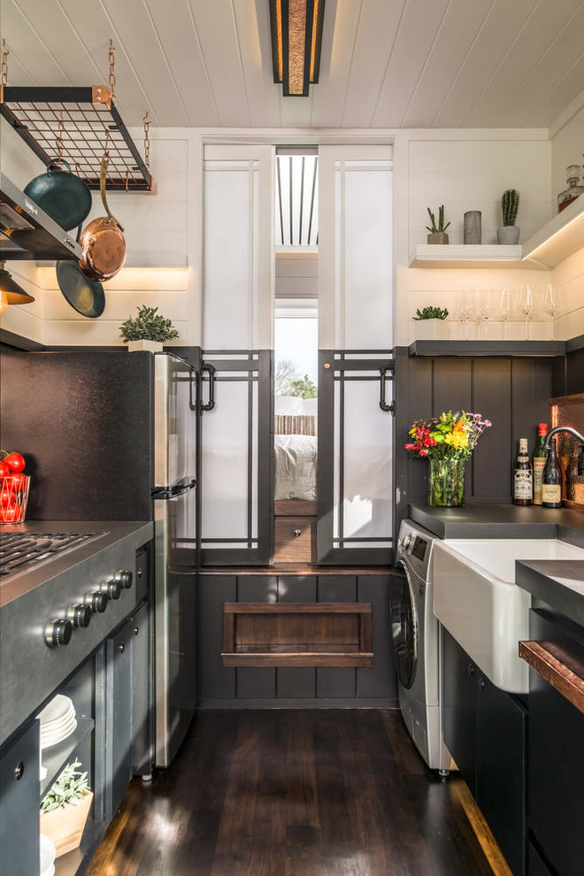 Inspiration for an industrial galley dark wood floor and brown floor kitchen remodel in Nashville with a farmhouse sink, flat-panel cabinets, black cabinets, black backsplash, no island and black countertops