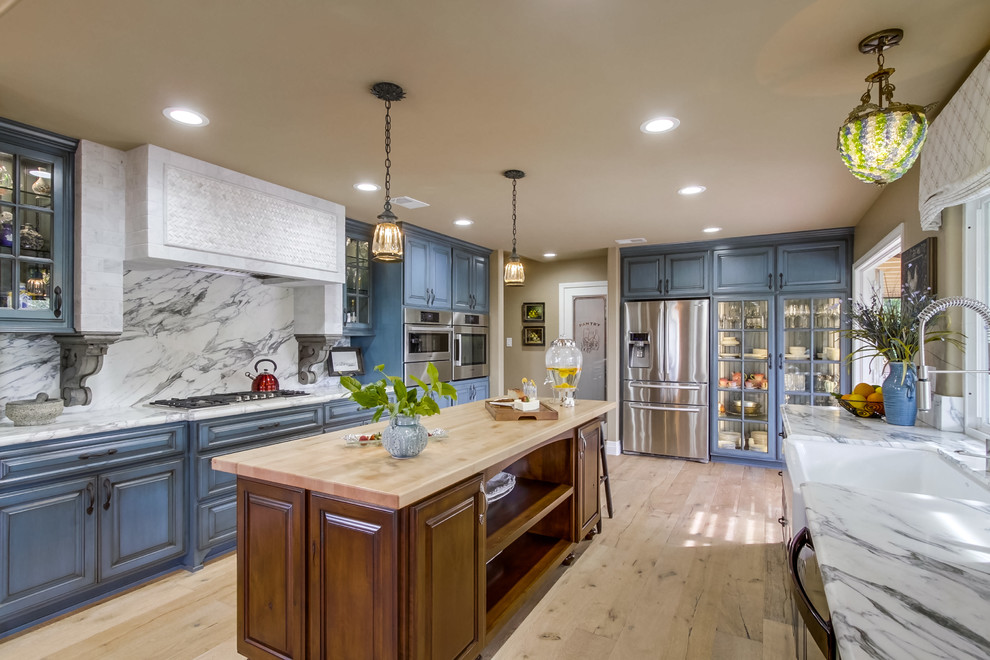 Inspiration for a classic u-shaped kitchen in San Diego with a belfast sink, raised-panel cabinets, blue cabinets, white splashback, stone slab splashback, stainless steel appliances, light hardwood flooring and an island.