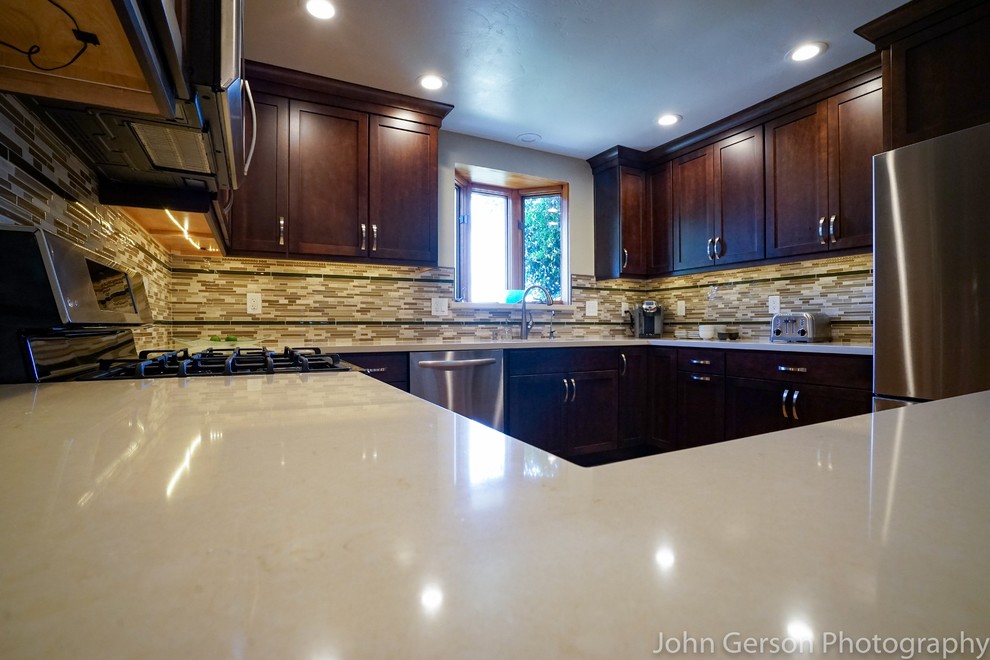 Large minimalist u-shaped light wood floor enclosed kitchen photo in San Diego with a double-bowl sink, recessed-panel cabinets, dark wood cabinets, quartzite countertops, brown backsplash, glass tile backsplash, stainless steel appliances and a peninsula