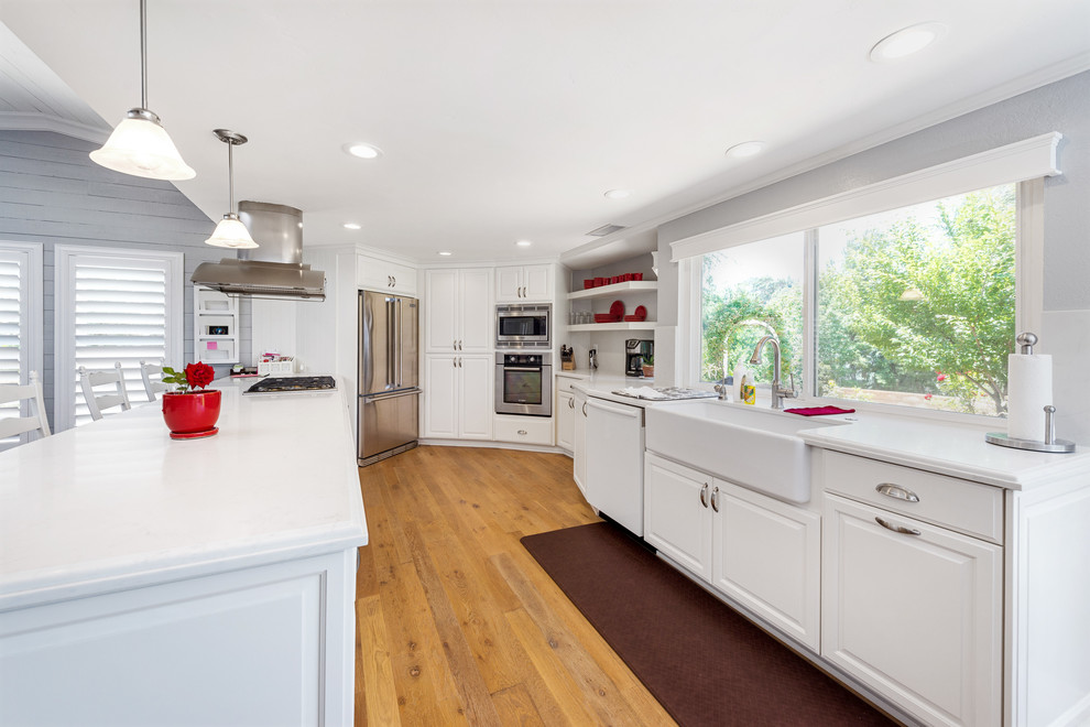 Open concept kitchen - large cottage single-wall light wood floor open concept kitchen idea in San Diego with a farmhouse sink, raised-panel cabinets, white cabinets, quartz countertops, white backsplash, stainless steel appliances and a peninsula