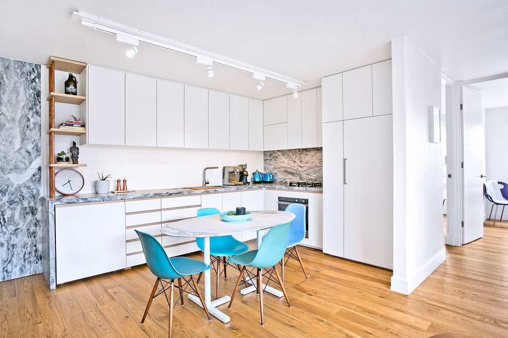 This is an example of a small contemporary l-shaped kitchen/diner in Sydney with a double-bowl sink, flat-panel cabinets, white cabinets, marble worktops, white splashback, marble splashback, black appliances, medium hardwood flooring, no island, brown floors and grey worktops.