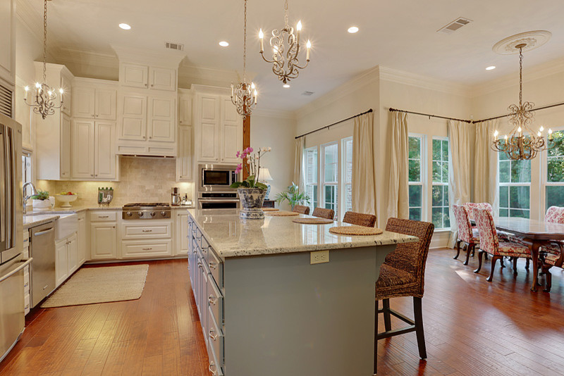 Inspiration for a large timeless l-shaped medium tone wood floor open concept kitchen remodel in New Orleans with raised-panel cabinets, white cabinets, granite countertops, beige backsplash, stone tile backsplash, stainless steel appliances and an island