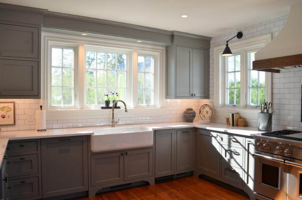Example of a classic medium tone wood floor kitchen design in Bridgeport with a farmhouse sink, beaded inset cabinets, brown cabinets, quartzite countertops, white backsplash, porcelain backsplash, paneled appliances and white countertops