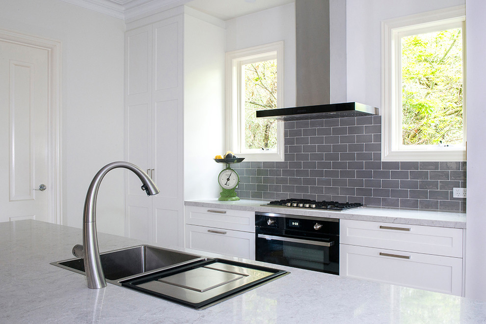 Inspiration for a large classic l-shaped open plan kitchen in Melbourne with a double-bowl sink, shaker cabinets, white cabinets, engineered stone countertops, grey splashback, metro tiled splashback, stainless steel appliances, medium hardwood flooring, an island, brown floors and grey worktops.