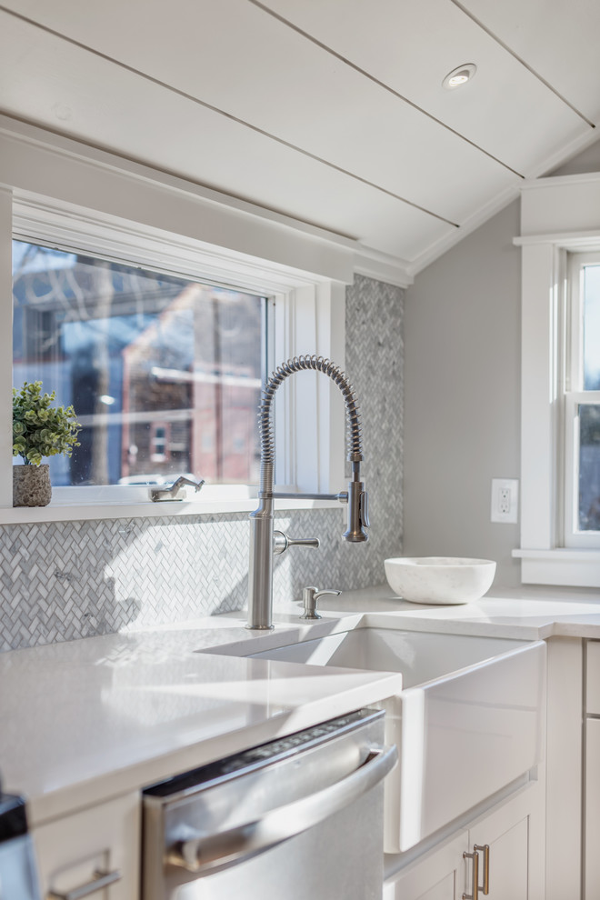 Inspiration for a small farmhouse l-shaped kitchen/diner in Boston with a belfast sink, shaker cabinets, white cabinets, engineered stone countertops, grey splashback, marble splashback, stainless steel appliances, light hardwood flooring, no island, beige floors and white worktops.
