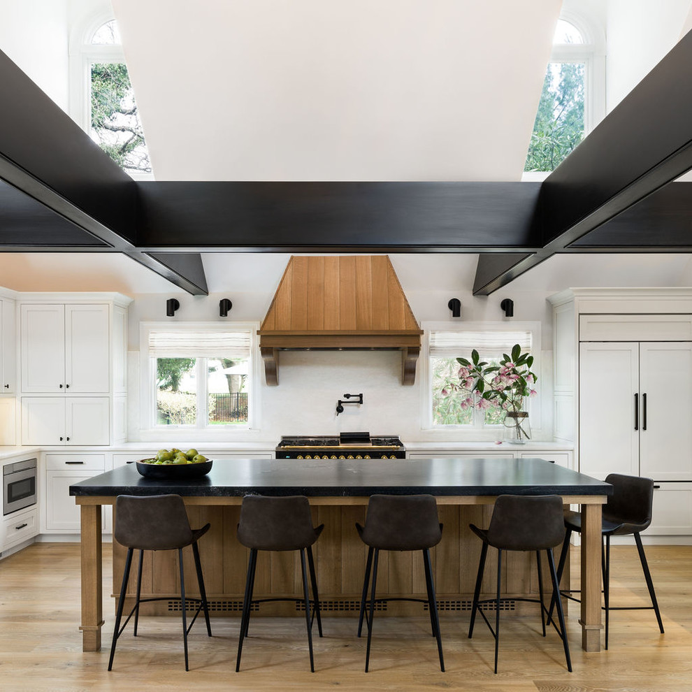 Inspiration for a transitional l-shaped medium tone wood floor and brown floor open concept kitchen remodel in Other with shaker cabinets, white cabinets, quartzite countertops, white backsplash, paneled appliances, an island and black countertops