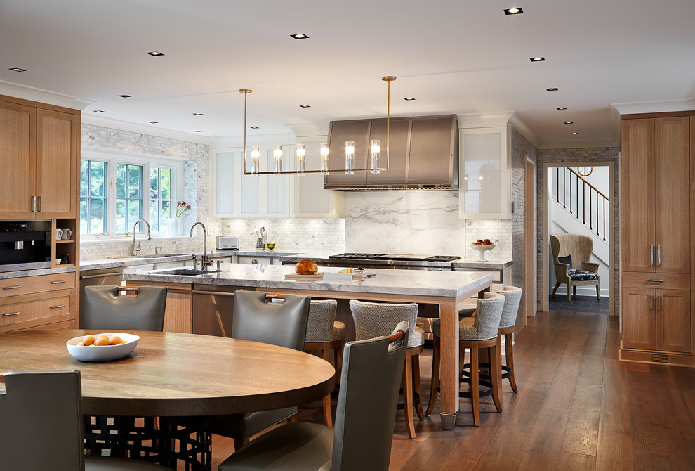 This is an example of a medium sized traditional l-shaped kitchen/diner in Chicago with a submerged sink, glass-front cabinets, white cabinets, marble worktops, grey splashback, stainless steel appliances, an island and dark hardwood flooring.