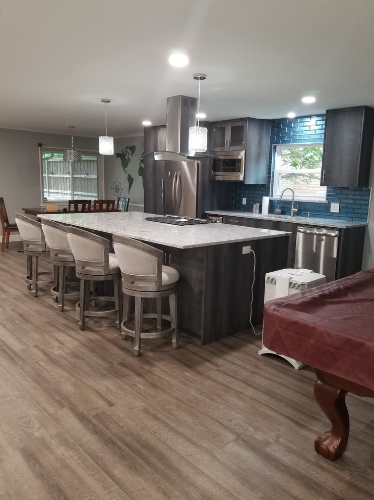 Foto på ett mellanstort vintage grå linjärt kök med öppen planlösning, med en undermonterad diskho, släta luckor, grå skåp, granitbänkskiva, blått stänkskydd, stänkskydd i glaskakel, rostfria vitvaror, laminatgolv, en köksö och brunt golv
