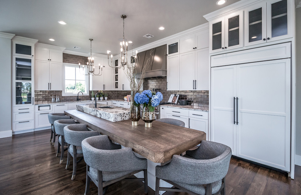 Huge transitional l-shaped medium tone wood floor and brown floor open concept kitchen photo in Other with an undermount sink, recessed-panel cabinets, white cabinets, granite countertops, gray backsplash, porcelain backsplash, paneled appliances, an island and multicolored countertops