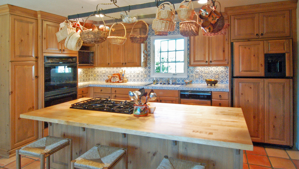 Inredning av ett amerikanskt mellanstort kök, med en undermonterad diskho, luckor med upphöjd panel, skåp i ljust trä, kaklad bänkskiva, blått stänkskydd, stänkskydd i keramik, svarta vitvaror, klinkergolv i terrakotta och en köksö