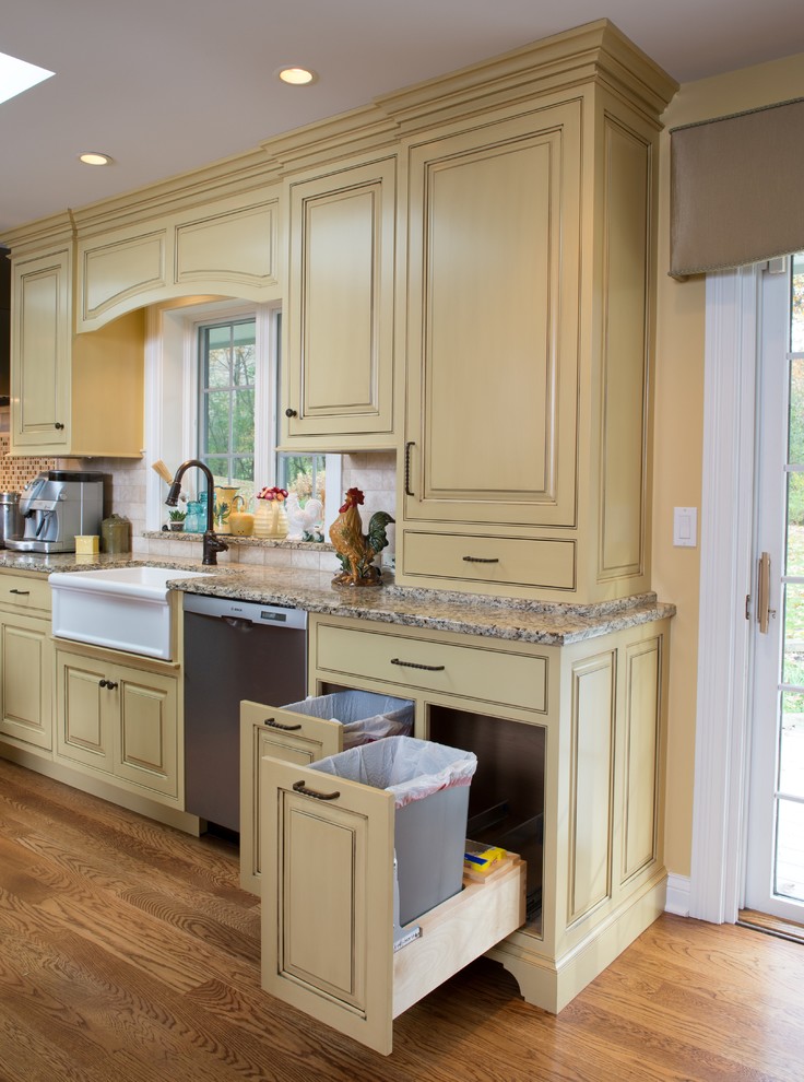 Elegant u-shaped eat-in kitchen photo in Chicago with a farmhouse sink, raised-panel cabinets, yellow cabinets, granite countertops, beige backsplash, stone tile backsplash and stainless steel appliances