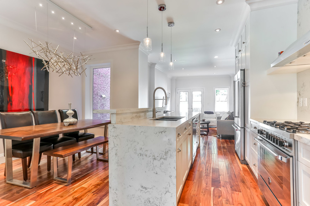Example of a mid-sized trendy single-wall medium tone wood floor eat-in kitchen design in Toronto with a double-bowl sink, shaker cabinets, white cabinets, quartz countertops, white backsplash, stainless steel appliances, an island and stone slab backsplash