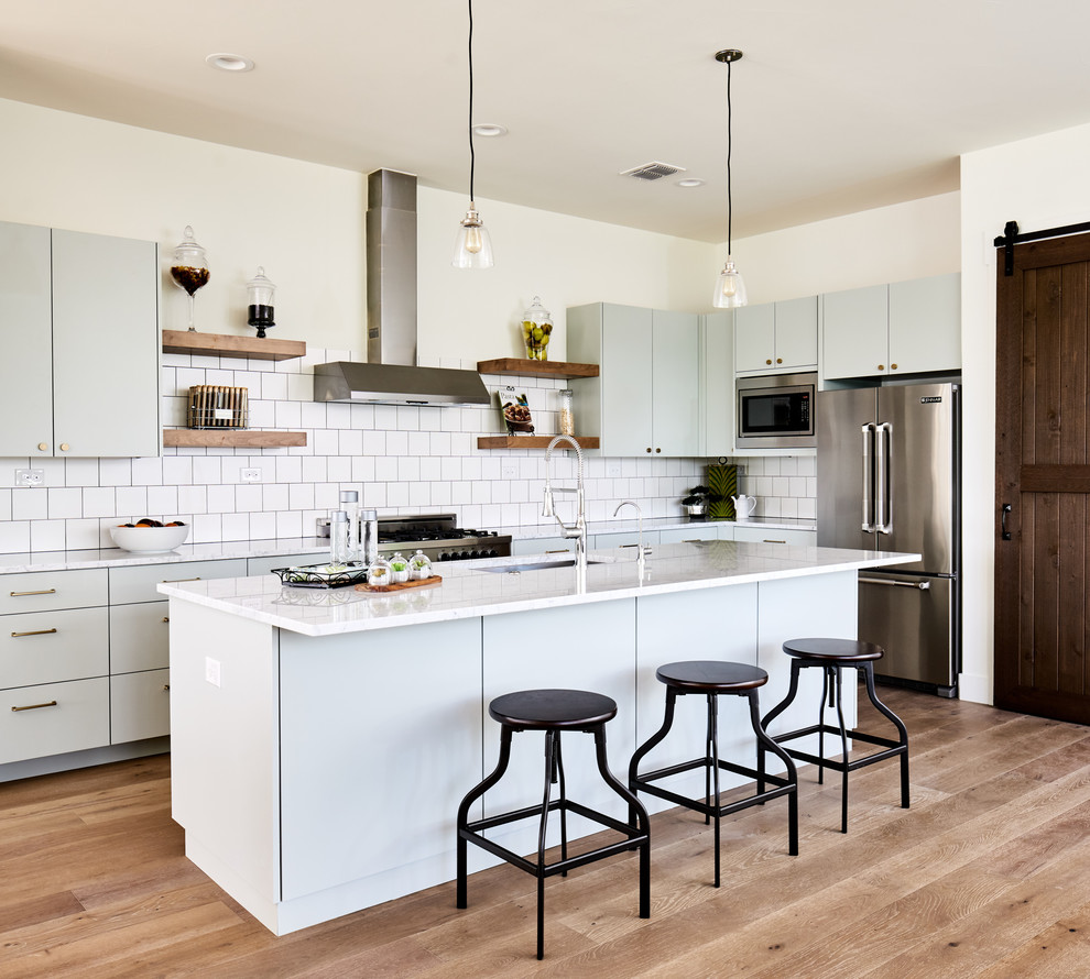 Example of a beach style light wood floor and beige floor kitchen design in Other with an undermount sink, flat-panel cabinets, gray cabinets, white backsplash, stainless steel appliances, an island and white countertops