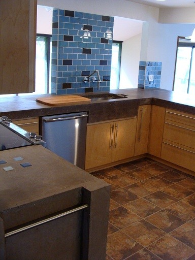 Modern inredning av ett mellanstort kök, med släta luckor, skåp i ljust trä, bänkskiva i betong, brunt stänkskydd, stänkskydd i glaskakel och rostfria vitvaror