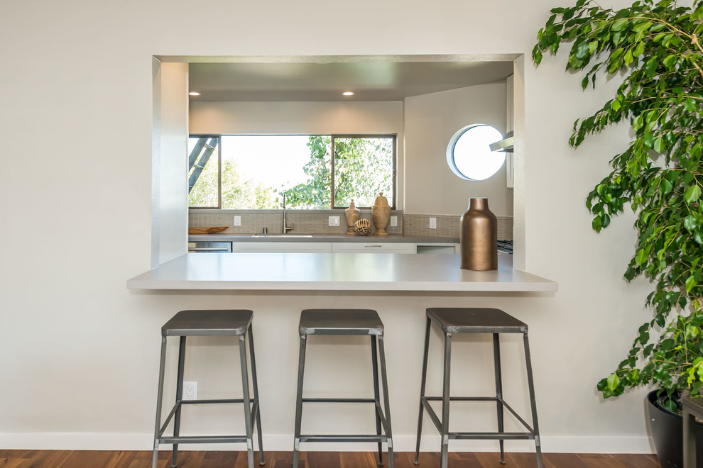 Modern inredning av ett litet grå grått kök, med en undermonterad diskho, skåp i shakerstil, vita skåp, bänkskiva i koppar, beige stänkskydd, stänkskydd i glaskakel, rostfria vitvaror, mellanmörkt trägolv, en halv köksö och brunt golv