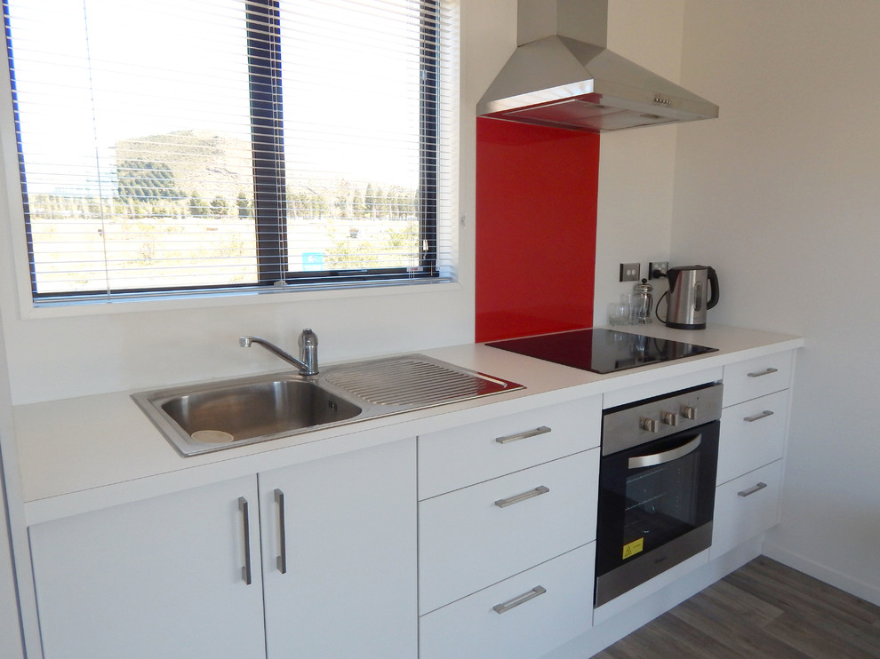 Exempel på ett litet modernt linjärt kök och matrum, med vita skåp, laminatbänkskiva, rött stänkskydd, glaspanel som stänkskydd, rostfria vitvaror och vinylgolv