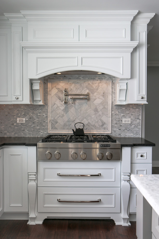 Cette image montre une cuisine traditionnelle avec des portes de placard blanches, un plan de travail en granite, une crédence grise, un électroménager en acier inoxydable, parquet foncé et îlot.