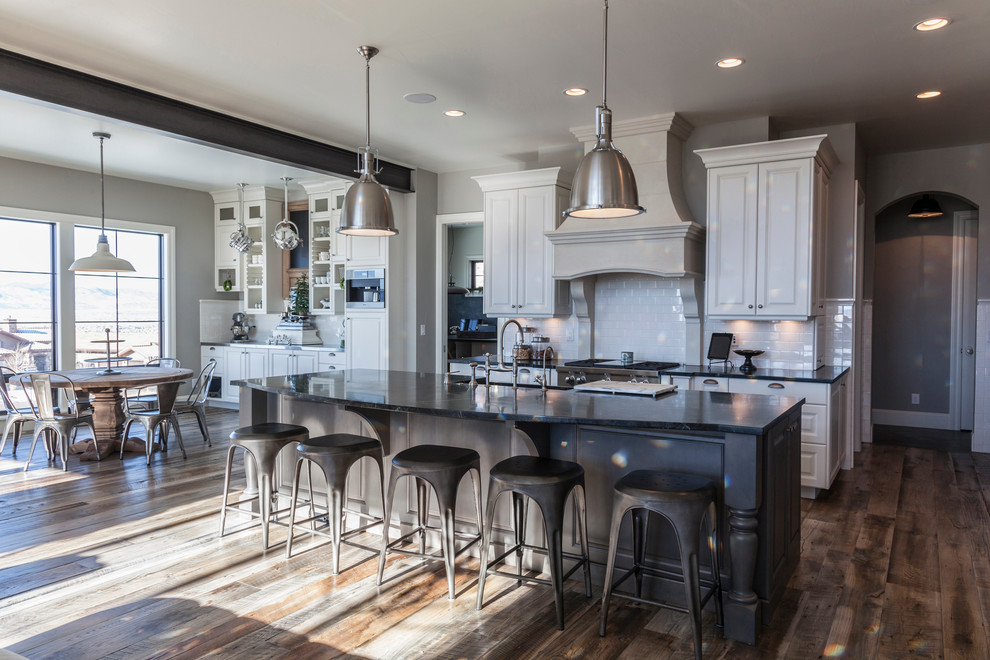 Inspiration for a huge industrial medium tone wood floor open concept kitchen remodel in Other with a farmhouse sink, raised-panel cabinets, white cabinets, soapstone countertops, white backsplash, ceramic backsplash and stainless steel appliances