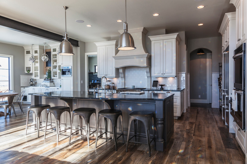 Huge urban medium tone wood floor open concept kitchen photo in Other with a farmhouse sink, raised-panel cabinets, white cabinets, soapstone countertops, white backsplash, ceramic backsplash and stainless steel appliances