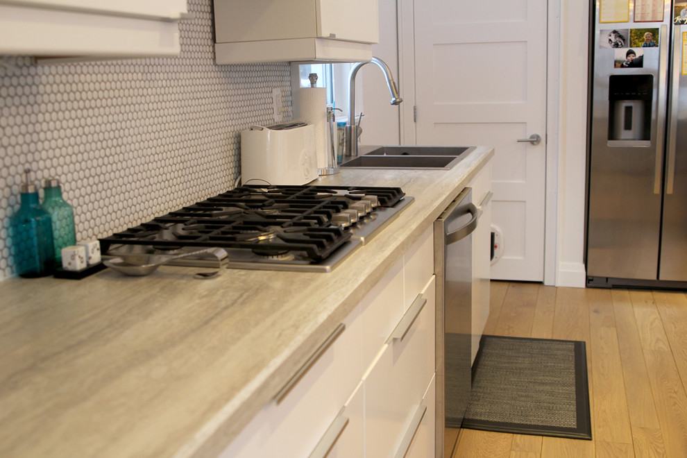 Example of a mid-sized trendy l-shaped light wood floor eat-in kitchen design in Calgary with a drop-in sink, flat-panel cabinets, white cabinets, laminate countertops, white backsplash, mosaic tile backsplash, stainless steel appliances and an island