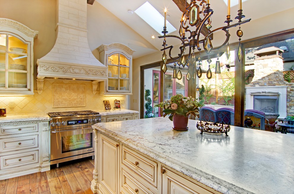 Immagine di una grande cucina chic con ante bianche, top in marmo, paraspruzzi beige, paraspruzzi con piastrelle in ceramica, elettrodomestici da incasso e pavimento in legno massello medio