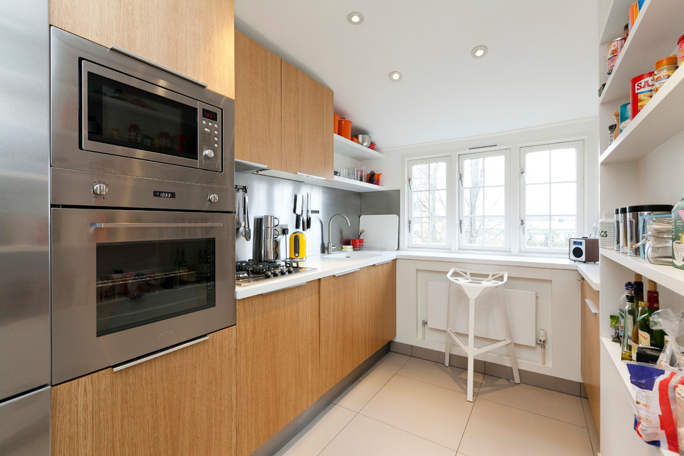 Photo of a small contemporary galley kitchen in London with an integrated sink, flat-panel cabinets, light wood cabinets, metallic splashback, stainless steel appliances and no island.