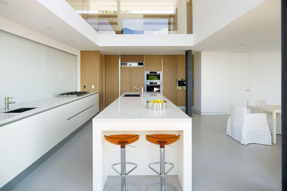Idéer för ett mellanstort modernt kök, med en undermonterad diskho, släta luckor, vita skåp, marmorbänkskiva, vitt stänkskydd, glaspanel som stänkskydd, rostfria vitvaror, betonggolv, en köksö och grått golv