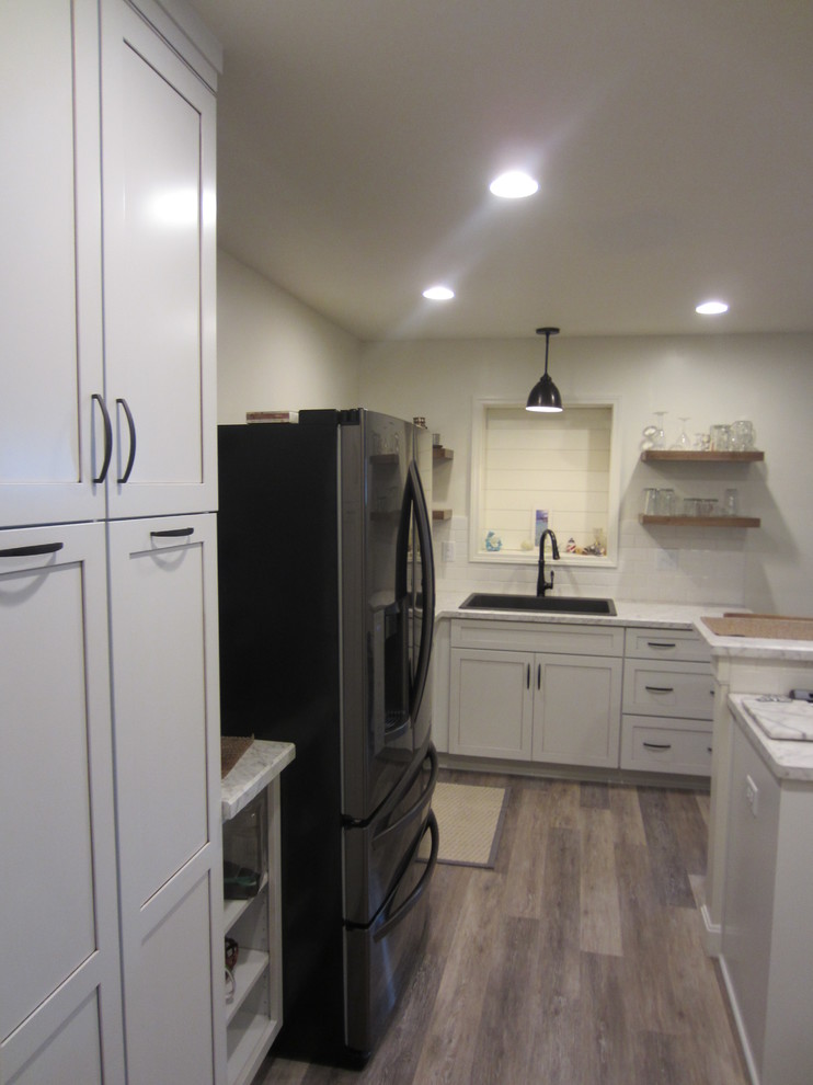 Idéer för ett litet lantligt vit kök, med en enkel diskho, skåp i shakerstil, vita skåp, laminatbänkskiva, vitt stänkskydd, stänkskydd i keramik, svarta vitvaror, laminatgolv, en halv köksö och grått golv