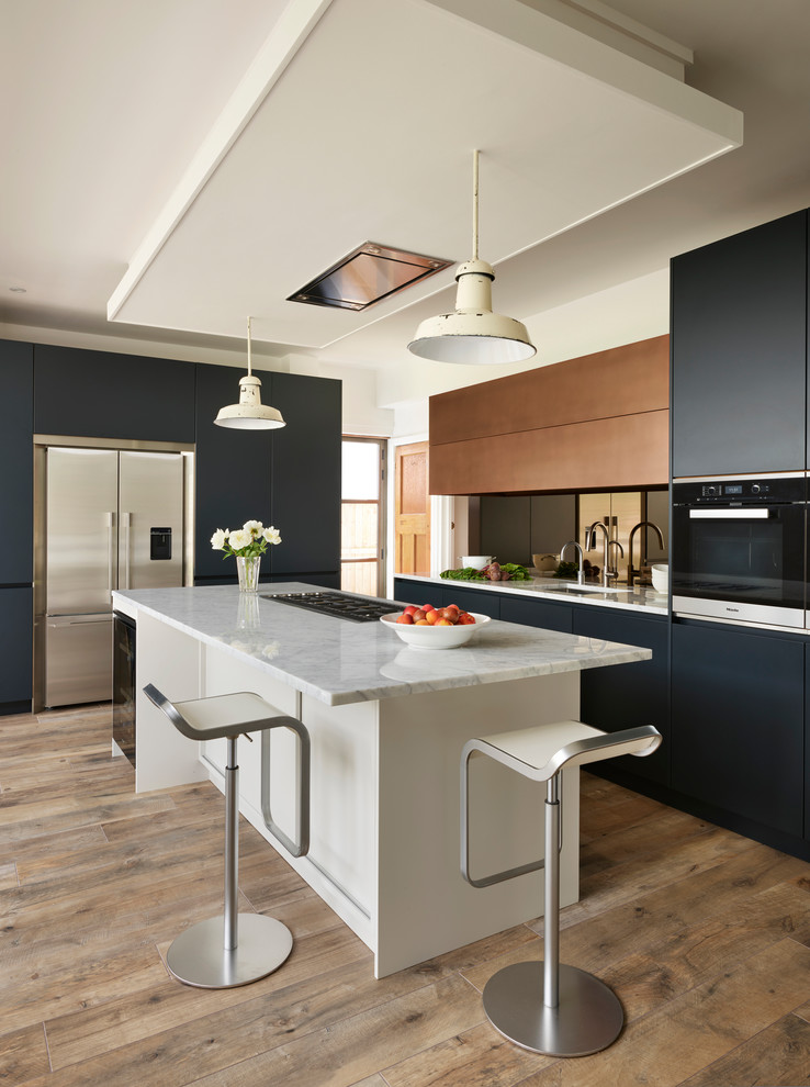Inspiration for a large contemporary l-shaped kitchen/diner in London with an integrated sink, blue cabinets, marble worktops, metallic splashback, mirror splashback, light hardwood flooring, an island, brown floors and white worktops.