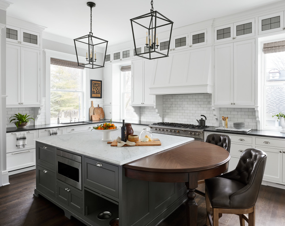 Transitional u-shaped dark wood floor and brown floor kitchen photo in Chicago with an undermount sink, recessed-panel cabinets, white cabinets, marble countertops, white backsplash, subway tile backsplash, stainless steel appliances, an island and black countertops