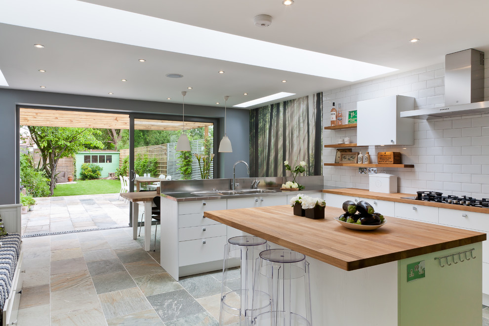 Mittelgroße Moderne Wohnküche mit integriertem Waschbecken, flächenbündigen Schrankfronten, weißen Schränken, Arbeitsplatte aus Holz, Küchenrückwand in Weiß, Kücheninsel und Rückwand aus Metrofliesen in Surrey