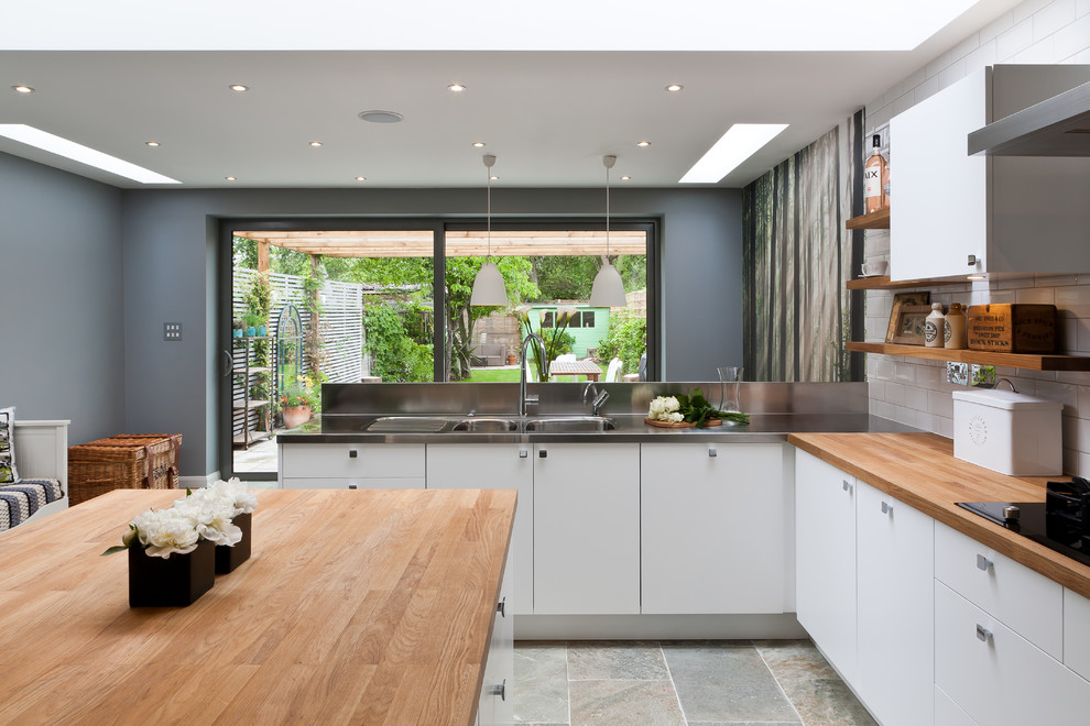 This is an example of a medium sized contemporary kitchen/diner in Surrey with an integrated sink, flat-panel cabinets, white cabinets, wood worktops, white splashback, ceramic splashback, stainless steel appliances and an island.