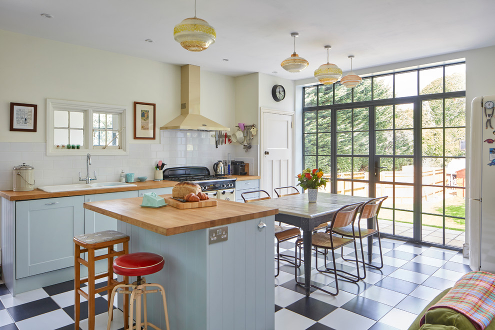 Offene Stilmix Küche mit Schrankfronten im Shaker-Stil, blauen Schränken, Arbeitsplatte aus Holz, Kücheninsel, Doppelwaschbecken, Küchenrückwand in Weiß, Rückwand aus Metrofliesen und buntem Boden in Oxfordshire