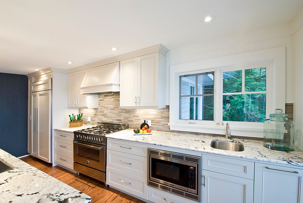 Modern inredning av ett stort linjärt kök med öppen planlösning, med en undermonterad diskho, skåp i shakerstil, vita skåp, granitbänkskiva, beige stänkskydd, stänkskydd i glaskakel, vita vitvaror, mellanmörkt trägolv och en köksö