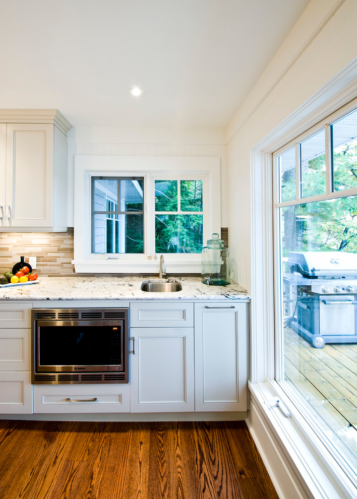 Foto på ett stort funkis linjärt kök med öppen planlösning, med en undermonterad diskho, skåp i shakerstil, vita skåp, granitbänkskiva, beige stänkskydd, stänkskydd i glaskakel, vita vitvaror, mellanmörkt trägolv och en köksö