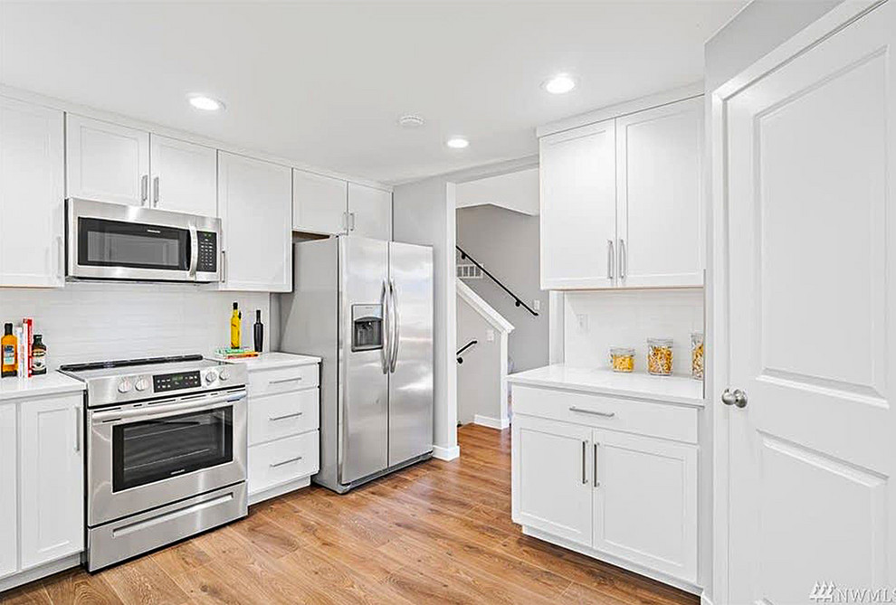 Imagen de cocina actual con puertas de armario blancas, salpicadero de azulejos de porcelana, suelo de madera en tonos medios y encimeras blancas