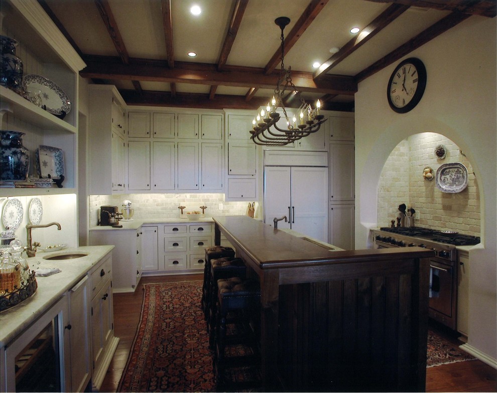 Immagine di una cucina ad U mediterranea chiusa con lavello sottopiano, ante bianche, paraspruzzi bianco, elettrodomestici da incasso, top in legno e struttura in muratura