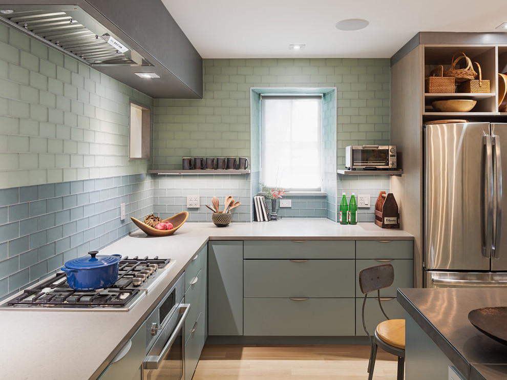 Design ideas for a contemporary l-shaped kitchen in Philadelphia with flat-panel cabinets, green cabinets, green splashback, glass tiled splashback, stainless steel appliances, light hardwood flooring, an island, beige floors and grey worktops.