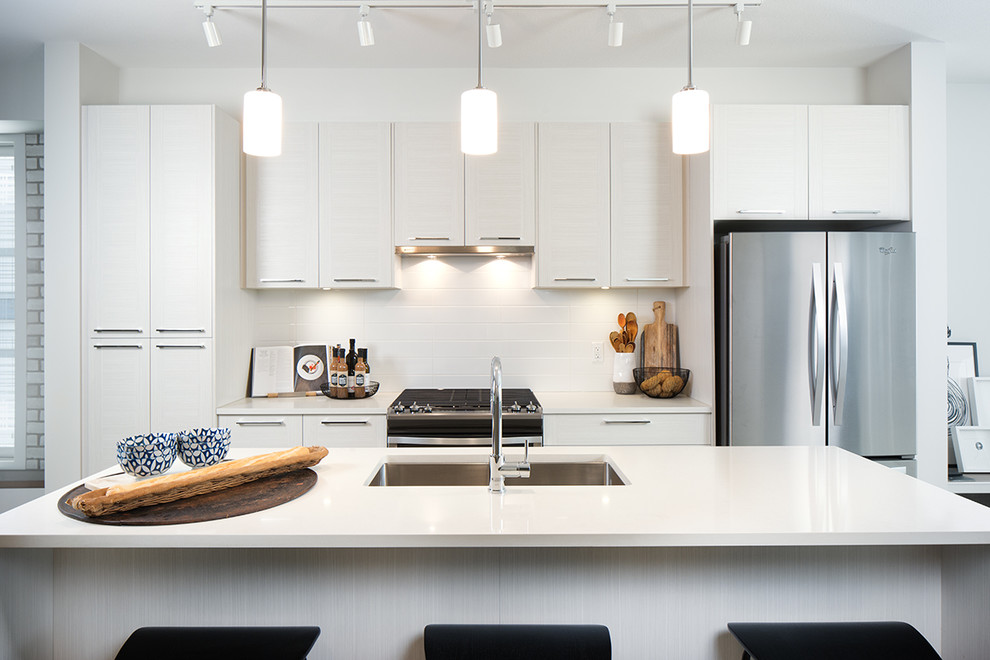 This is an example of a medium sized traditional galley kitchen/diner in Vancouver with a submerged sink, flat-panel cabinets, white cabinets, quartz worktops, white splashback, ceramic splashback, stainless steel appliances, medium hardwood flooring and an island.